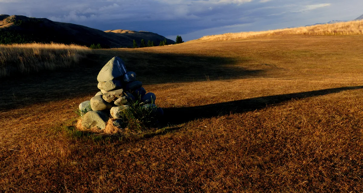 A stone cairn casting a long evening shadow across golden tussock