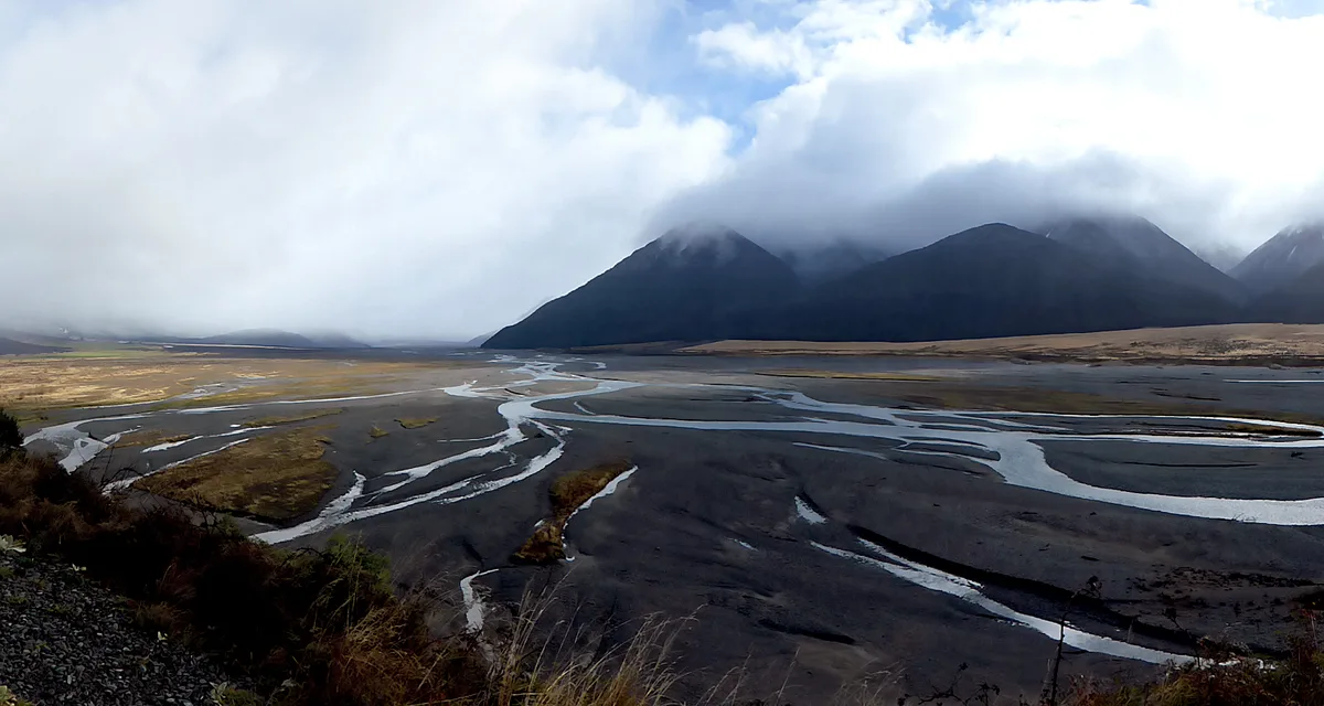 A braided river splitting into channels across a dark valley floor